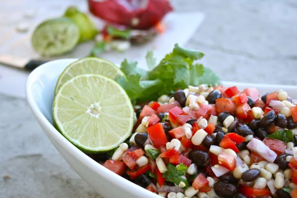 Side view of southwest black bean salad in a white dish, garnished with limes and cilantro.