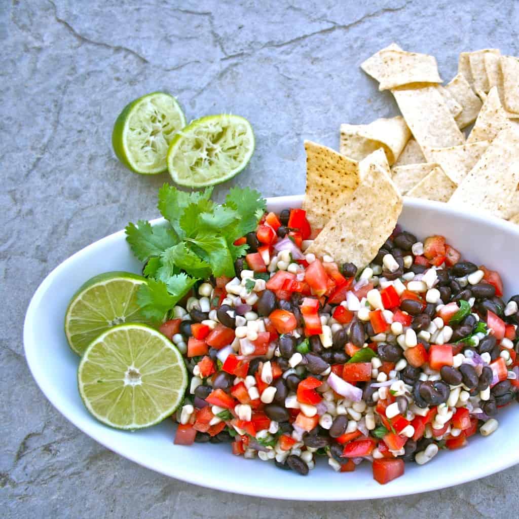 Overhead shot of southwest black bean salad in a white dish, garnished with limes, cilantro, and chips