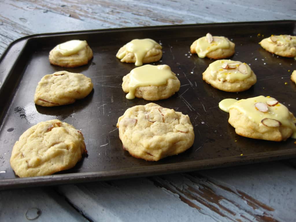 glazed and unglazed orange almond vegan cookies on dark baking sheet