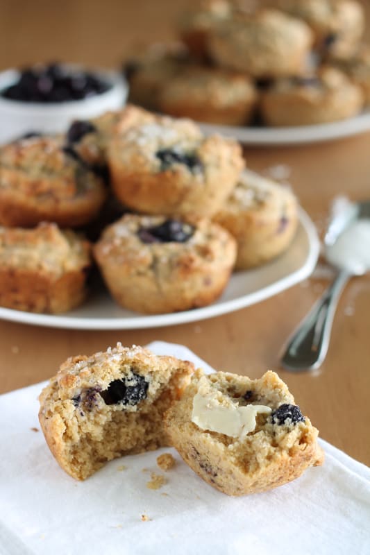 vegan blueberry muffin cut in half with pat of butter on it, sitting on white napkin
