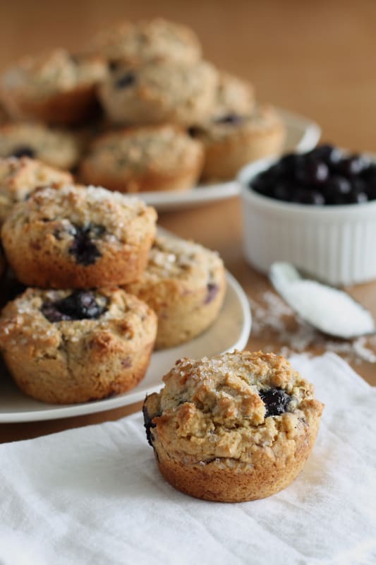 vegan blueberry muffin on white napkin with white plate of muffins in the background