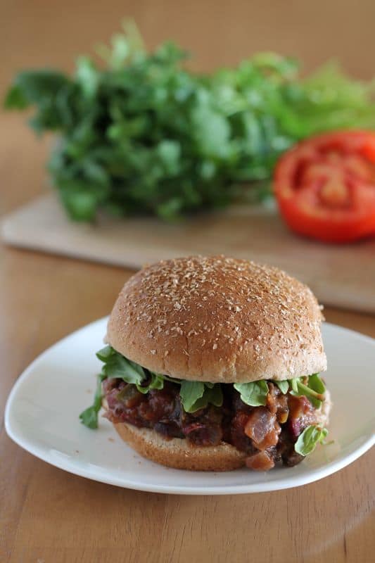 vegan sloppy joes on burger bun on white plate with wood background