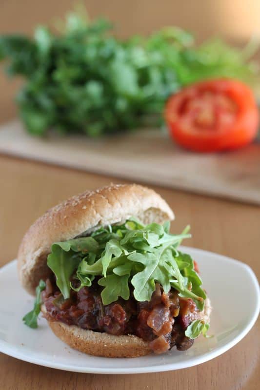 vegan sloppy joes on wheat bun with greens on white plate and wood background