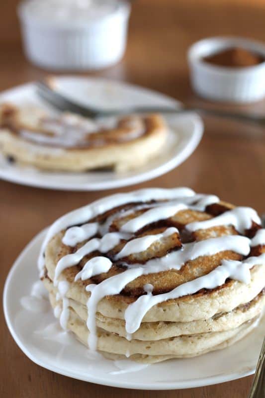 vegan cinnamon roll pancakes on white plate with coconut cream topping and wood background