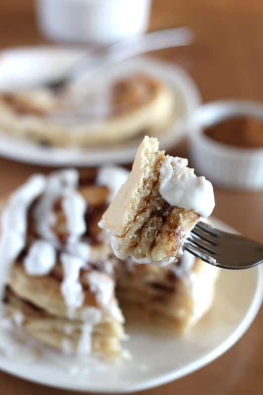 bite of vegan cinnamon roll pancake on white plate with coconut cream topping and wood background