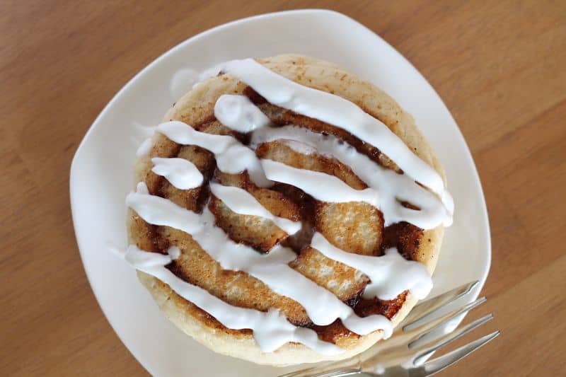 overhead shot of vegan cinnamon roll pancakes on white plate with coconut cream topping and wood background