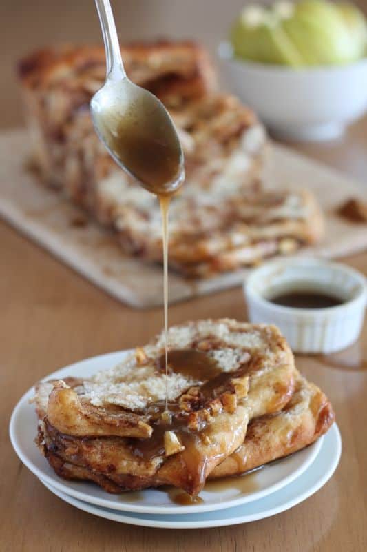 spoonful of vegan caramel being drizzled over vegan caramel apple pull apart bread on white plates with wood background
