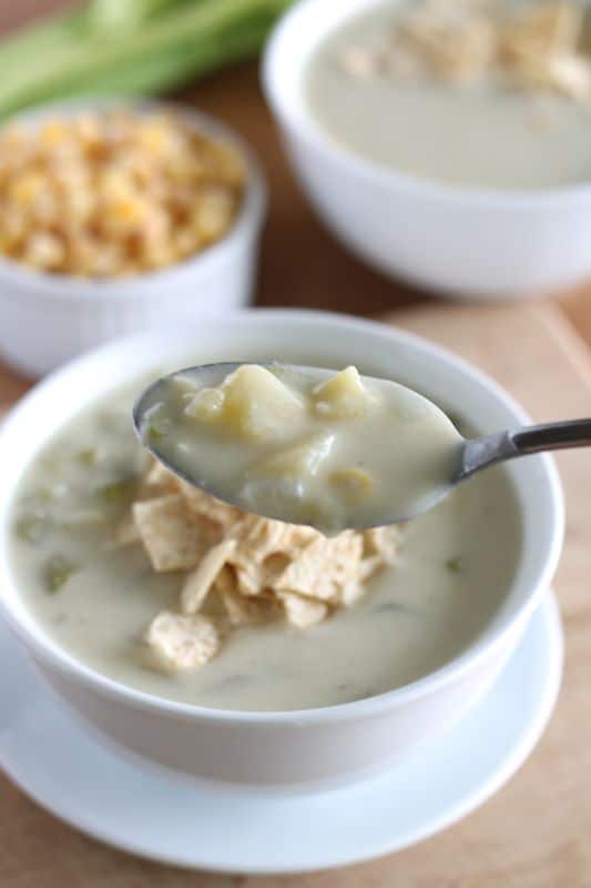 spoonful of vegan creamy potato soup with white bowl of soup in background