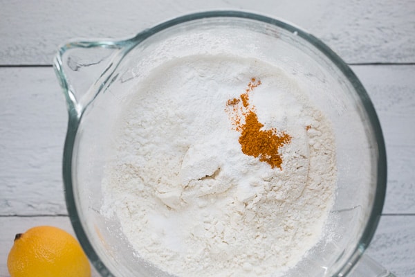 dry ingredients for vegan lemon bundt cake in clear glass mixing bowl with white shiplap background