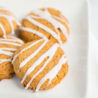 four pumpkin cookies with white icing in stripes on a white plate