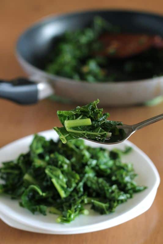 garlic cooked kale fork with white plate and skillet in background
