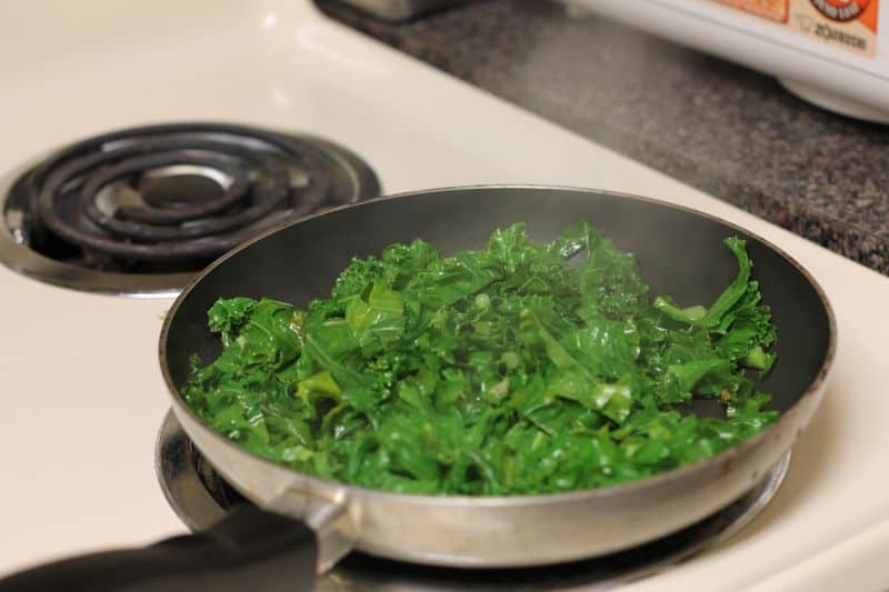 pre-seasoned garlic cooked kale in skillet on stovetop