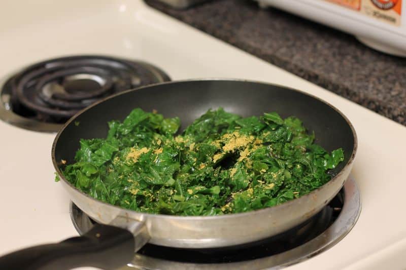 garlic cooked kale with nutritional yeast on top in skillet cooking on stovetop