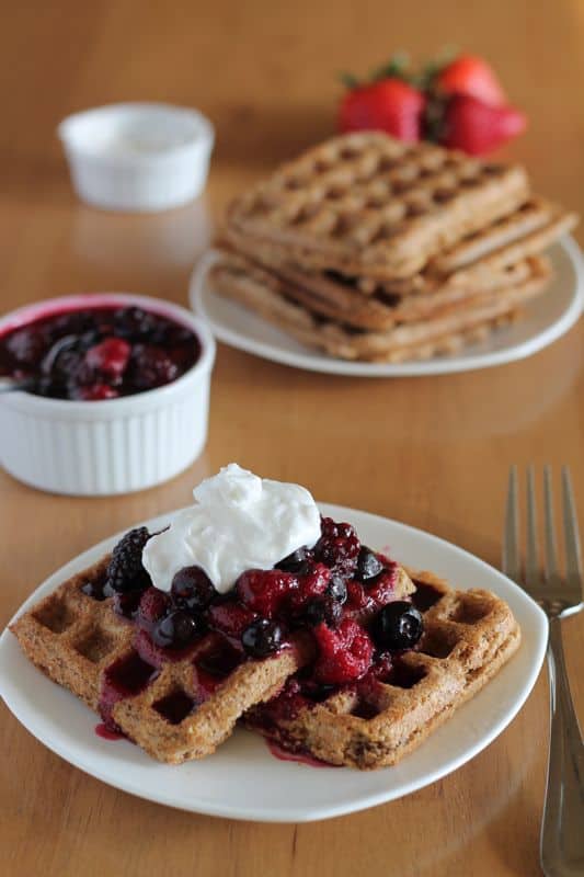 healthy vegan waffles with berry compote and coconut cream on white plate with wood background