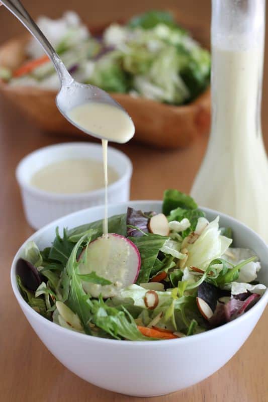 spoonful of vegan salad dressing being drizzled over salad