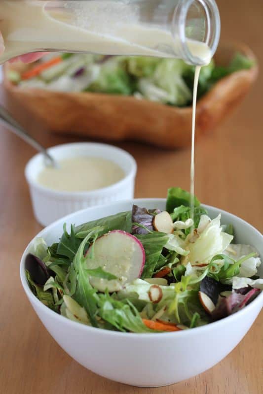 vegan salad dressing being poured over salad in white bowl