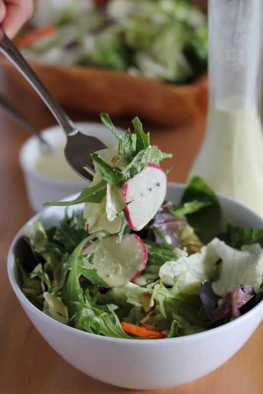 forkful of salad with vegan salad dressing in white bowl with wood background