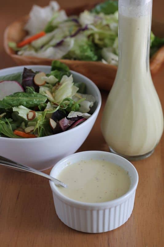 vegan salad dressing in white dish with salad and wooden background