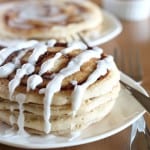 vegan cinnamon roll pancakes stacked on white plate with wood background