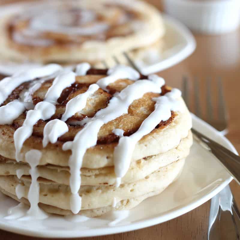 vegan cinnamon roll pancakes stacked on white plate with wood background