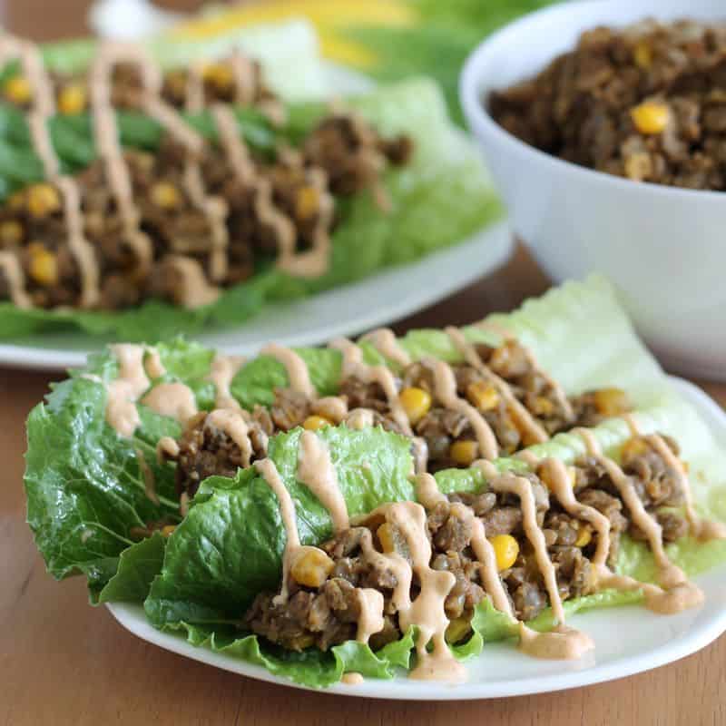 two vegan lentil lettuce tacos on small white plate with wooden background