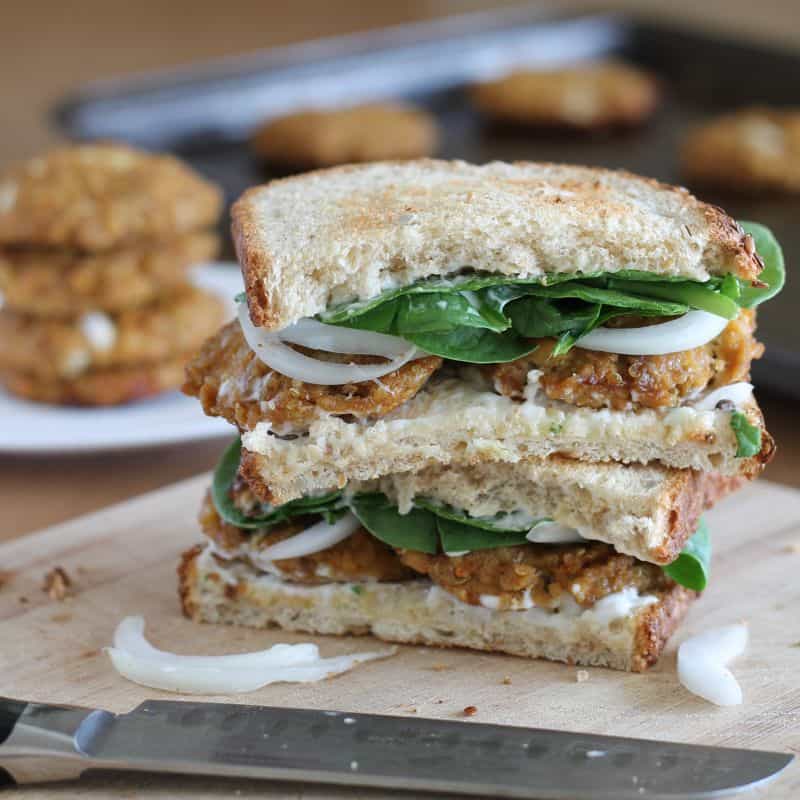 vegan tofu quinoa patties in sandwich with spinach and onion stacked on wood cutting board