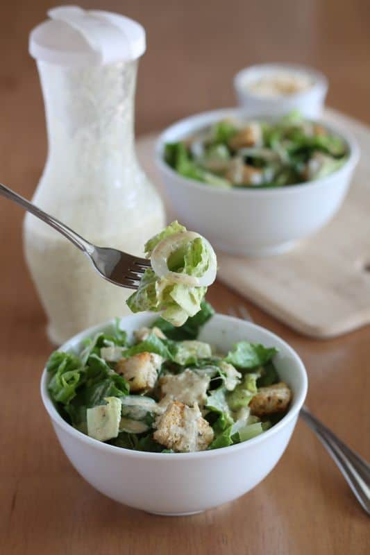 Vegan Caesar Salad in white bowl with forkful and wood background