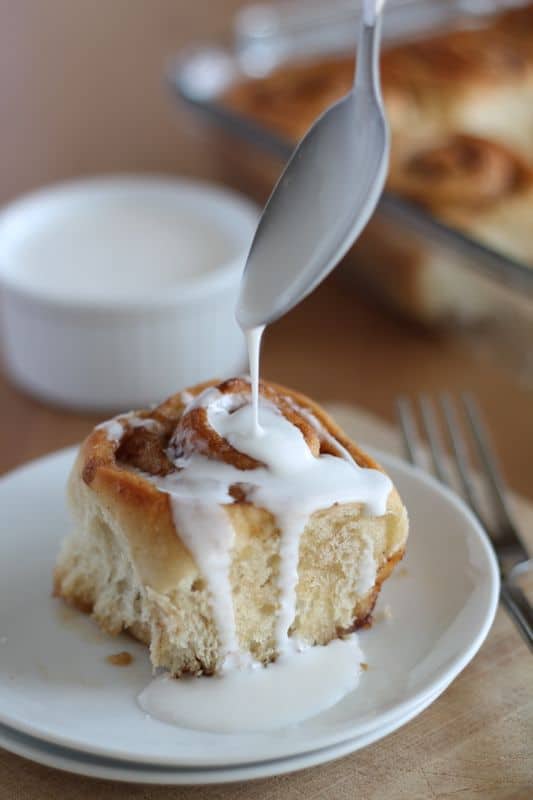 white coconut cream being spooned onto vegan cinnamon roll on white plate