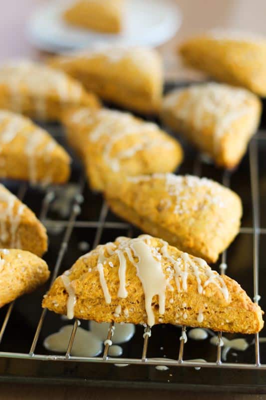 vegan pumpkin spice scones on cooling rack with icing dripping off the sides of scones