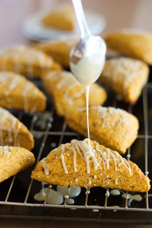 spoon drizzling maple icing over vegan pumpkin scones