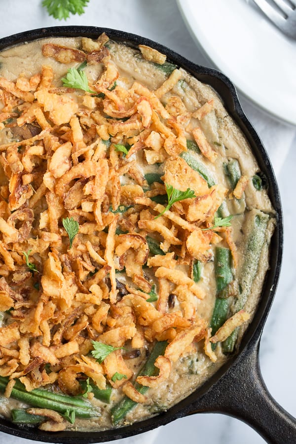 Vegan green bean casserole in a cast iron skillet with crispy French fried onions on top.