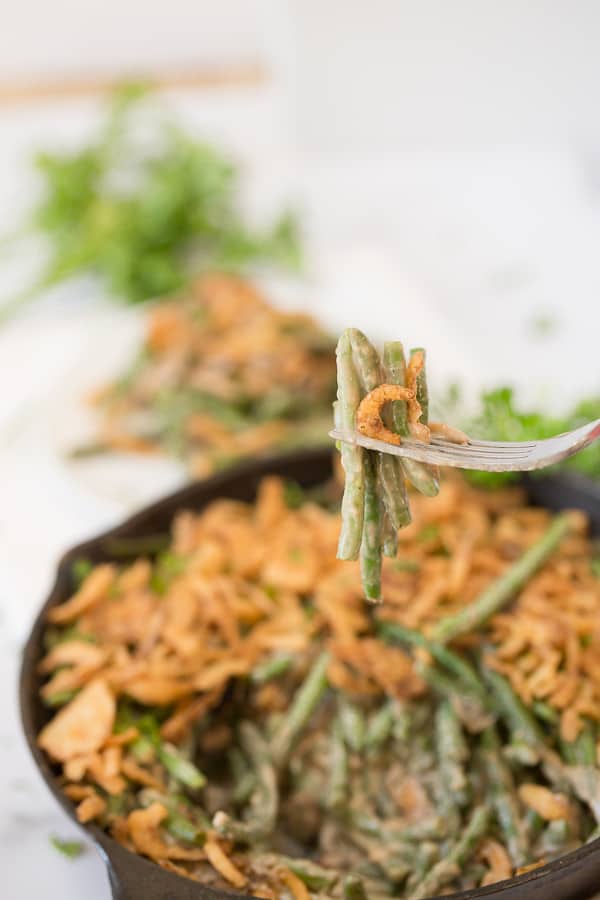 forkful of green bean casserole with full cast iron skillet in background