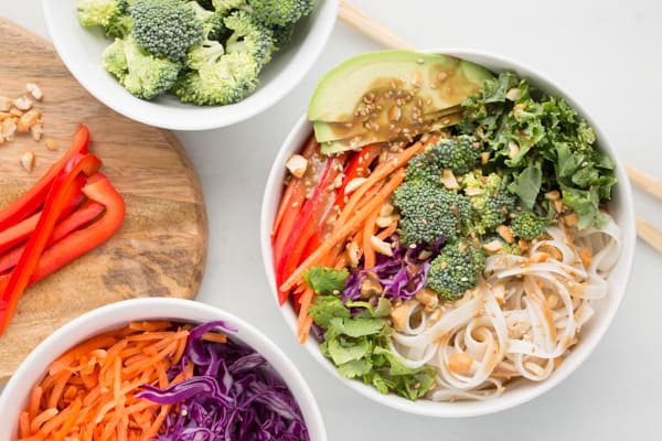 Vegan rainbow peanut noodle bowl with other vegetables in bowls and white background