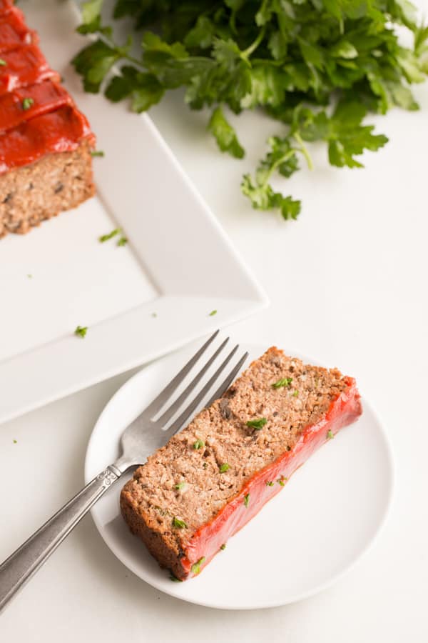 vegan meatloaf slice on a white plate with fork and parsley in the background