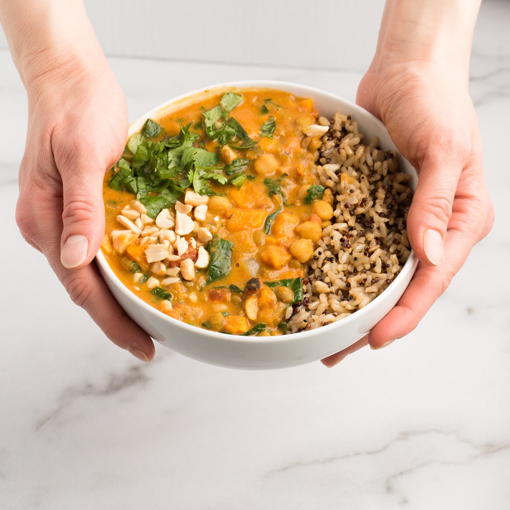 Vegan African Peanut stew in white bowl being held with caucasian hands with white marble background