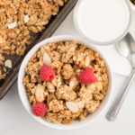 vegan almond butter granola garnished with raspberries in white bowl with white background