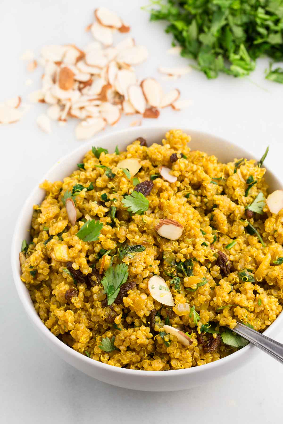 vegan curried quinoa in white bowl with white background, garnished with cilantro and sliced almonds