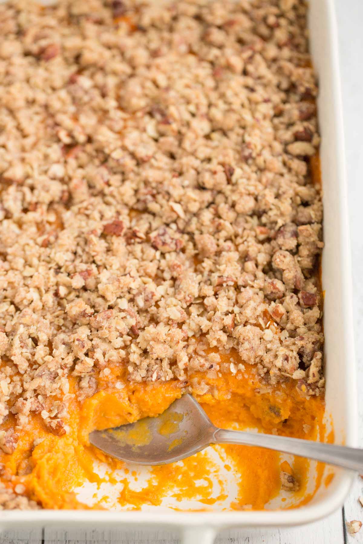 vegan sweet potato casserole with pecan crumble topping in gray and white casserole dish with metal spoon in dish